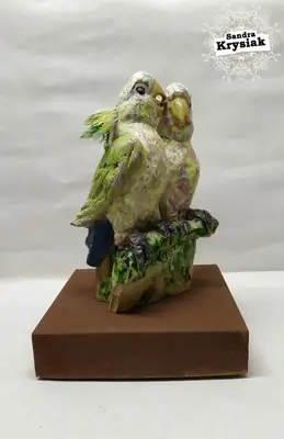 Escultura de dos aves verdes posadas sobre una base rectangular de madera