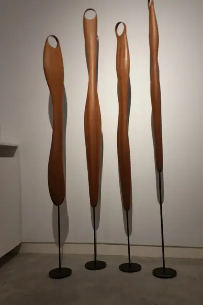 Cuatro esculturas verticales de madera oscura, con una abertura en lo alto, sobre pies negros