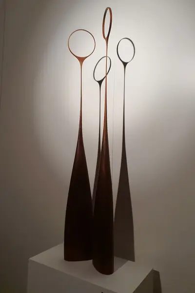 Tres esculturas altas de madera oscura con aros en lo alto, sobre peana blanca