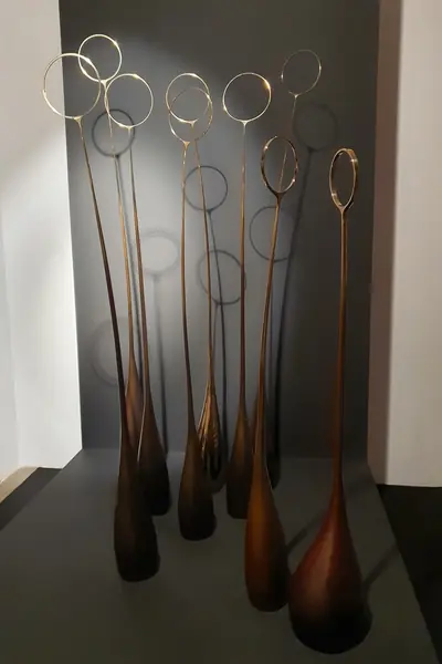 Grupo de piezas de madera rojiza, alargadas, con aros dorados en lo alto, en una sala de exposición