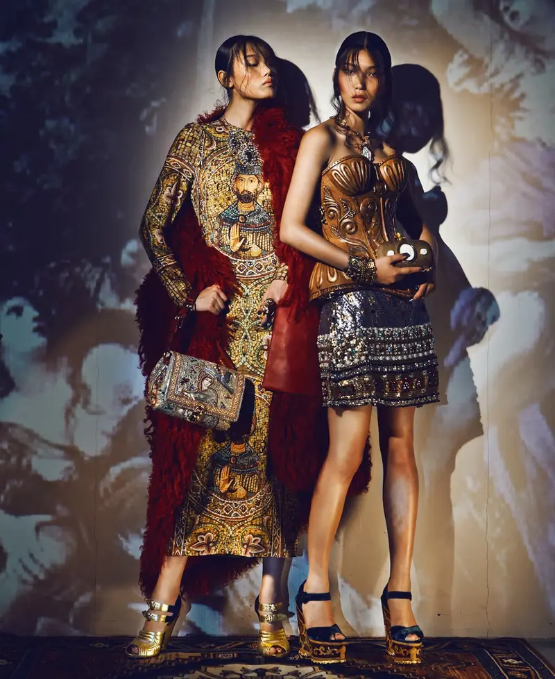 Dos modelos posan con abrigos de gala sobre corsés de madera tallada, en una editorial de moda fotografiada en penumbra