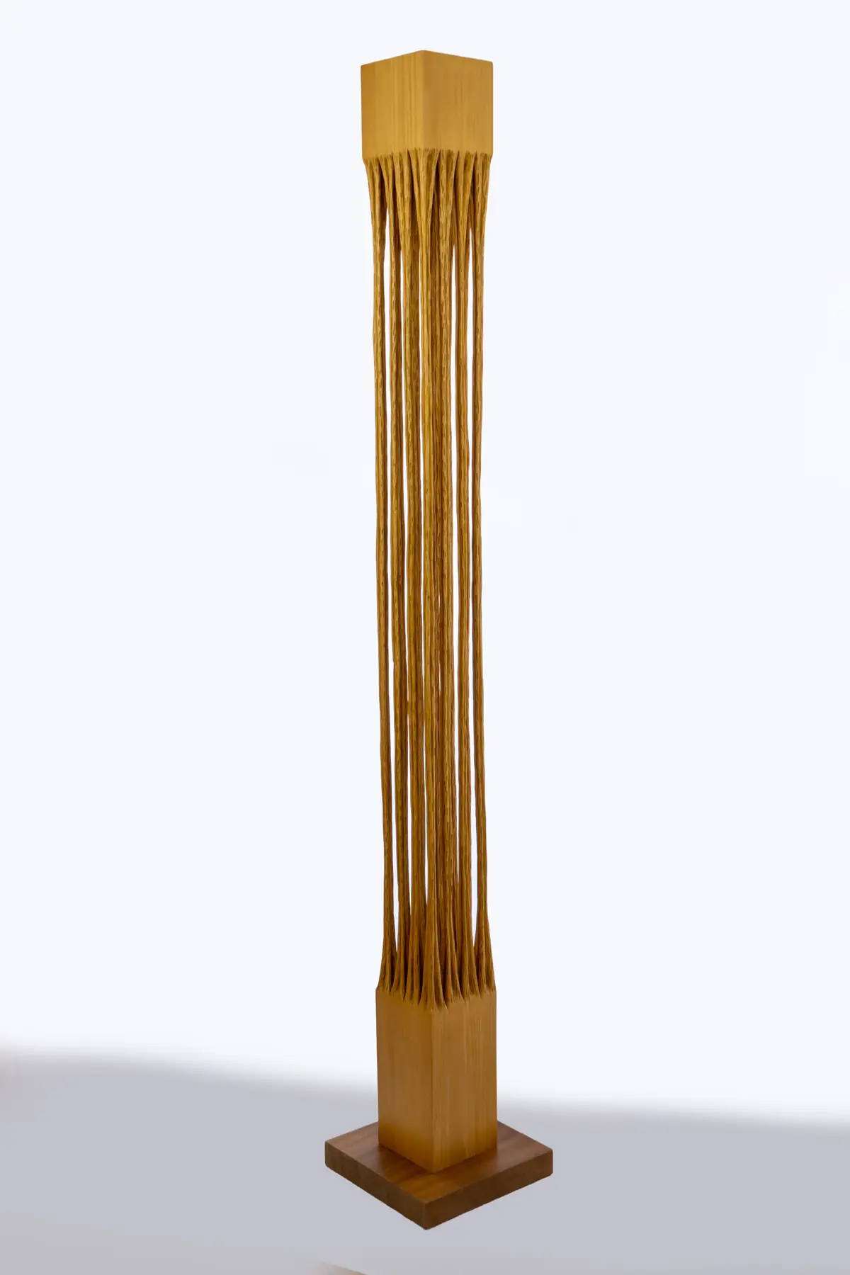 Columna vertical de ayous formada por cordones finos y paralelos que caen como raíces, sobre peana cuadrada