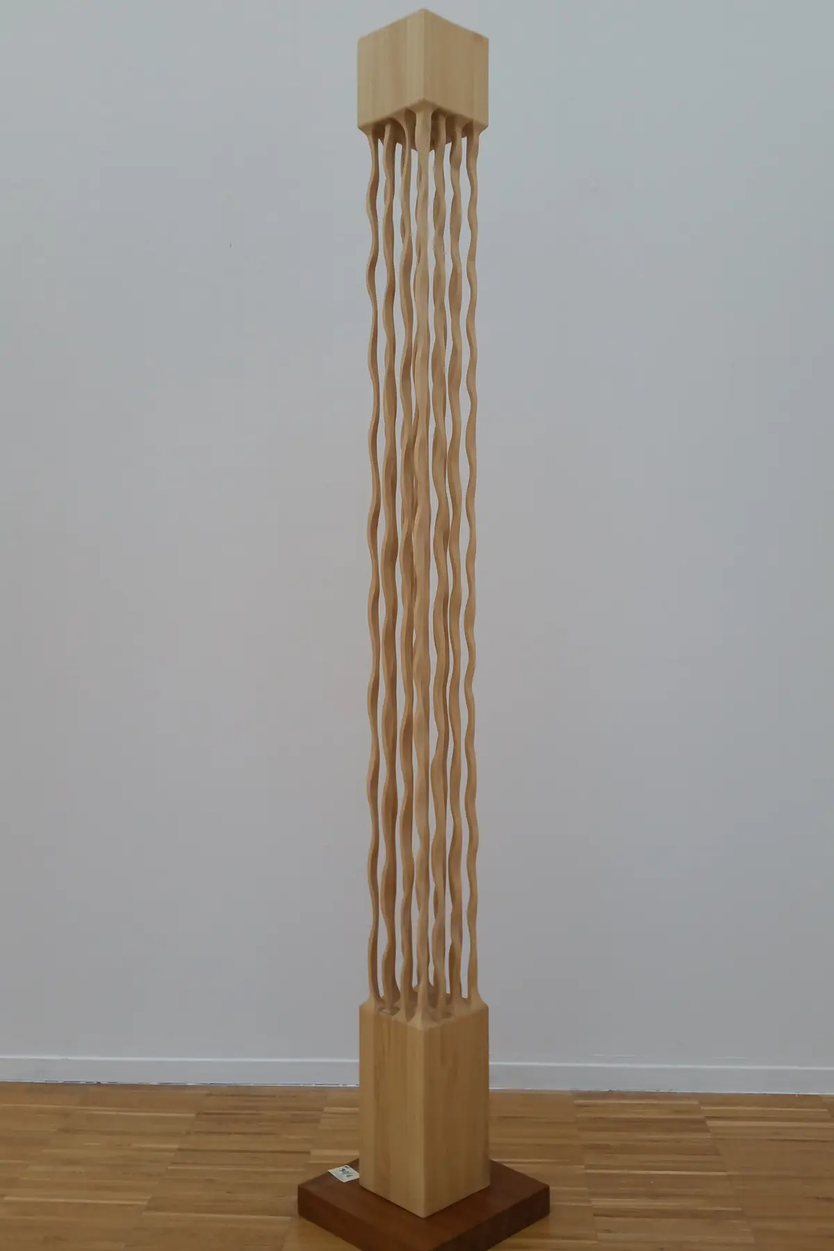 Columna vertical de ayous de cordones ondulados, apoyada en el suelo de una habitación de paredes claras