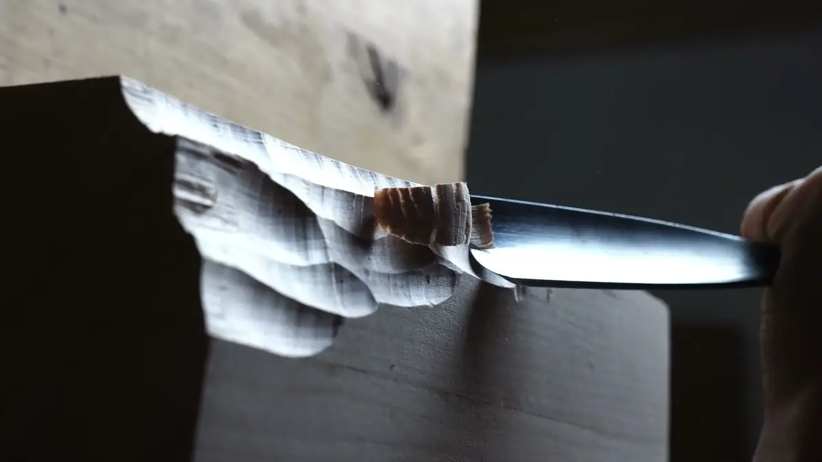 Manos sujetando una gubia y un mazo sobre una pieza de madera a medio tallar