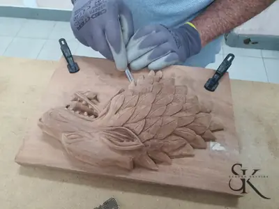 Manos trabajando con gubia en un relieve floral sujeto al banco