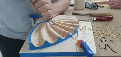 Manos tallando las formas de una concha de madera sujeta con sargentos
