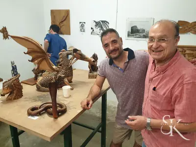 Dos alumnos muestran una pieza tallada junto a otras esculturas del taller