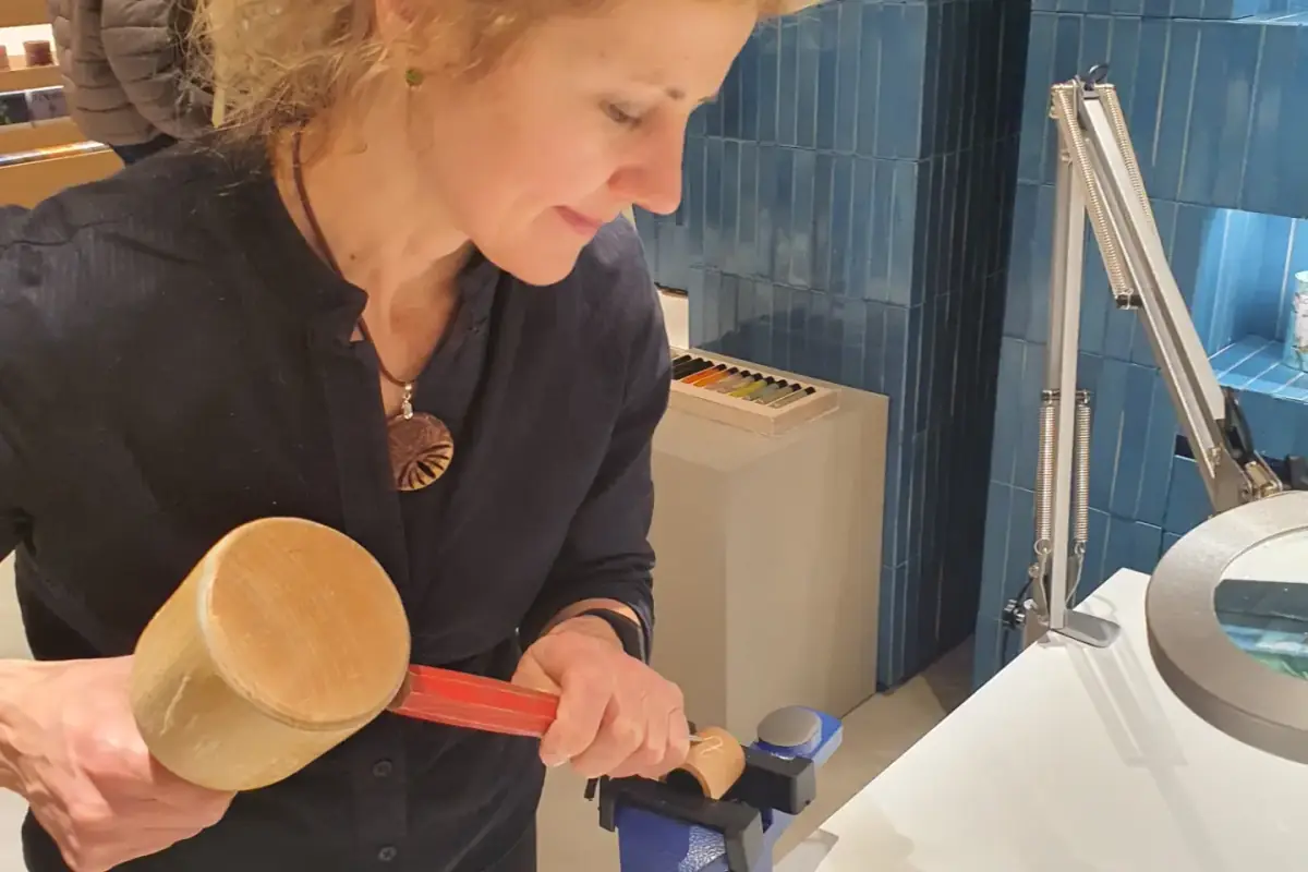 Sandra Krysiak tallando con mazo y gubia una pieza sujeta en un tornillo de mesa, en el mostrador de Loewe de El Corte Inglés