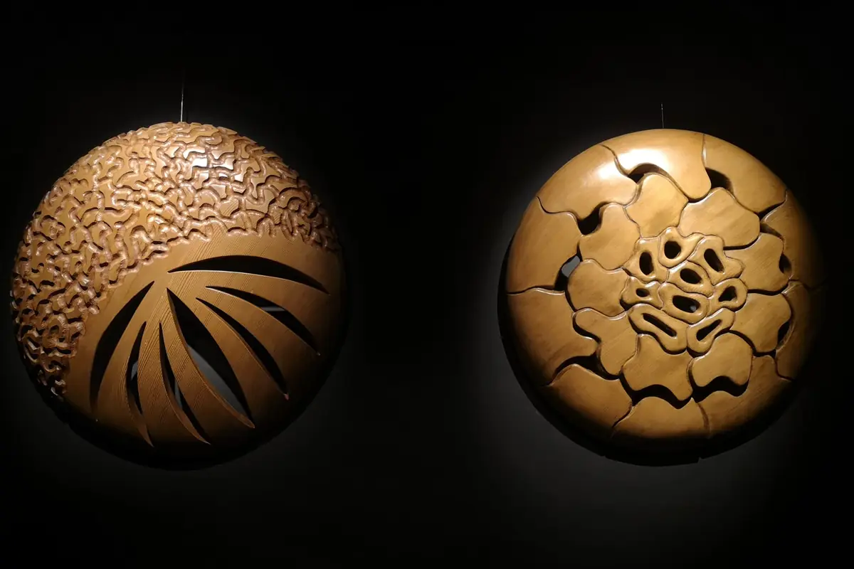 Dos relieves circulares de madera iluminados sobre la pared negra de la galería, en la exposición Quinteto