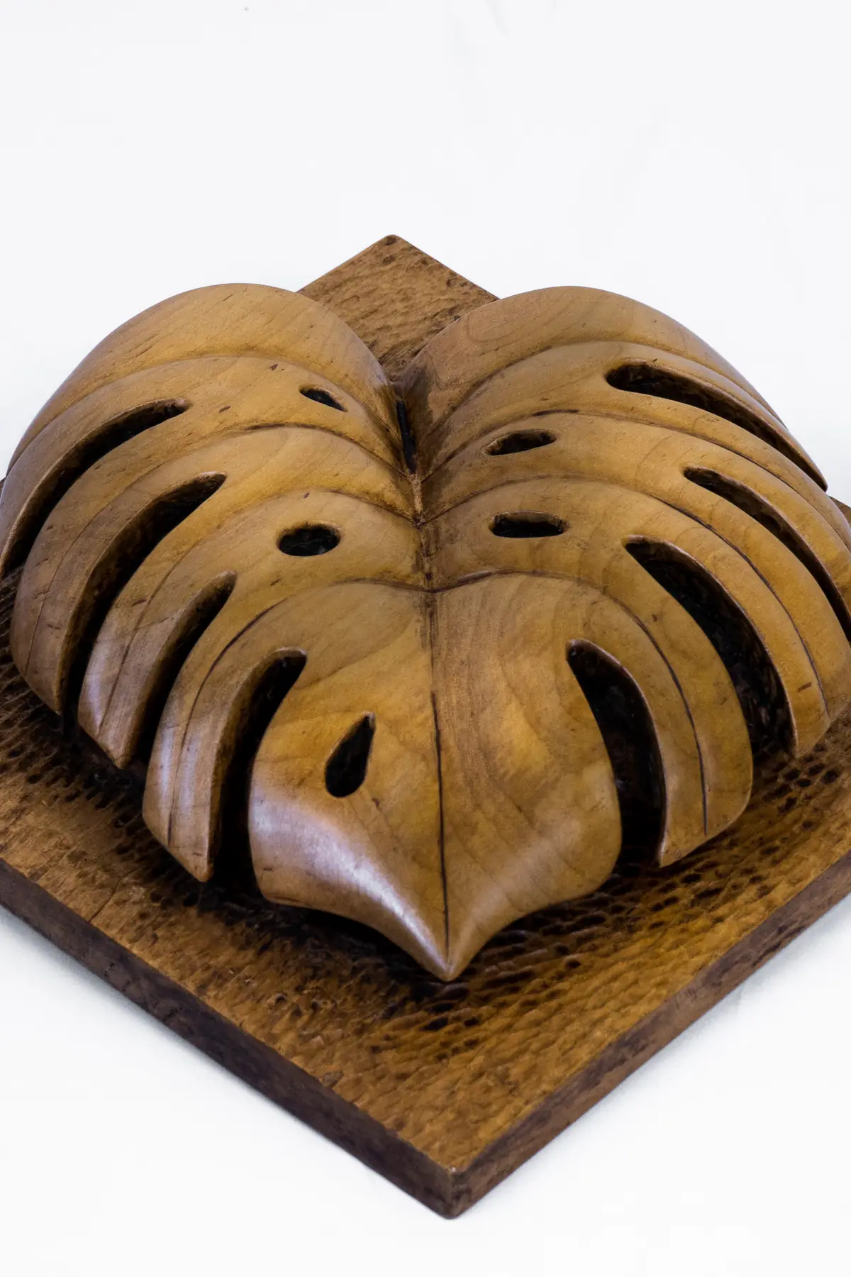 Relieve de una hoja tallada en madera sobre una base cuadrada, con la superficie pulida y hendiduras alargadas