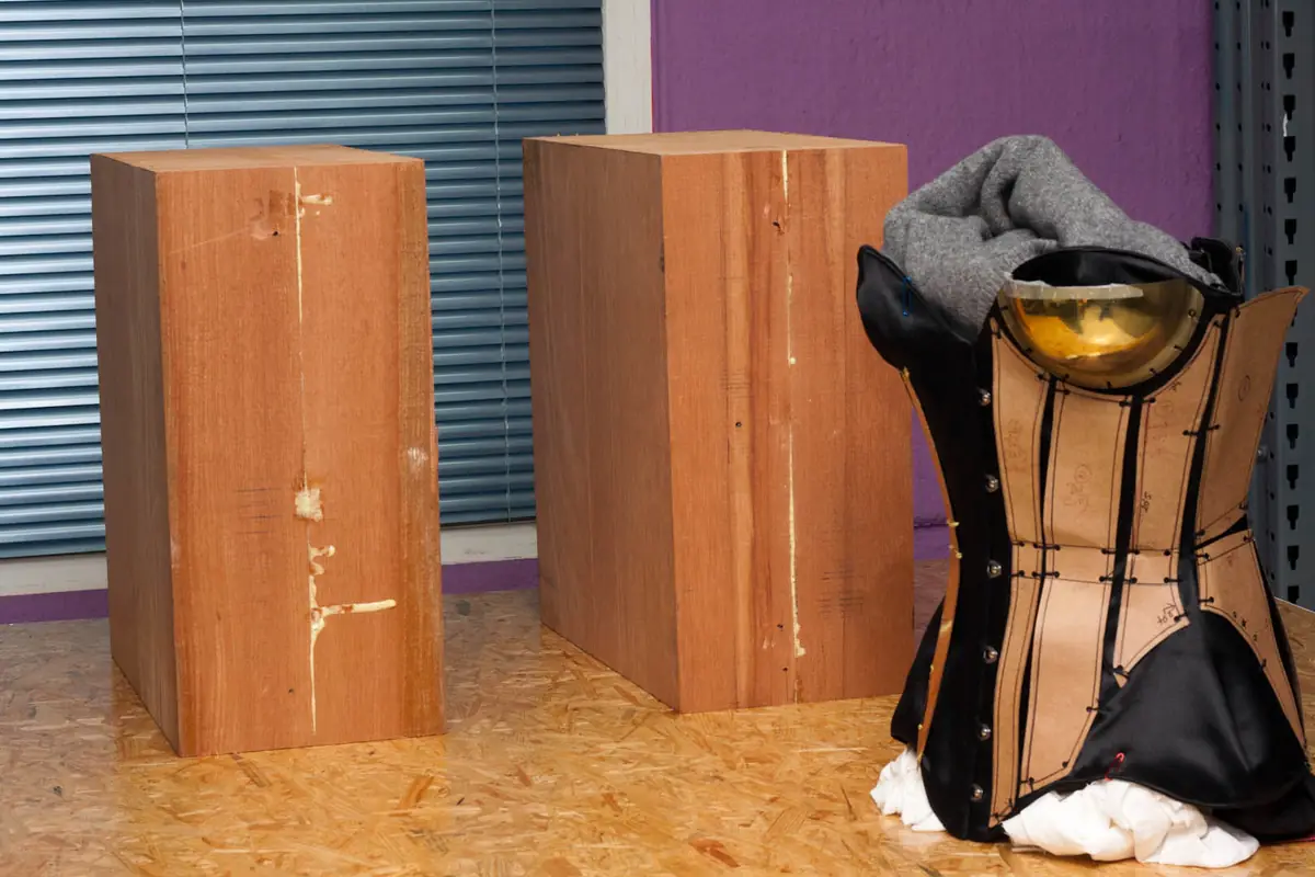 Dos bloques de madera en bruto junto al maniquí con el corsé de tela que sirve de referencia