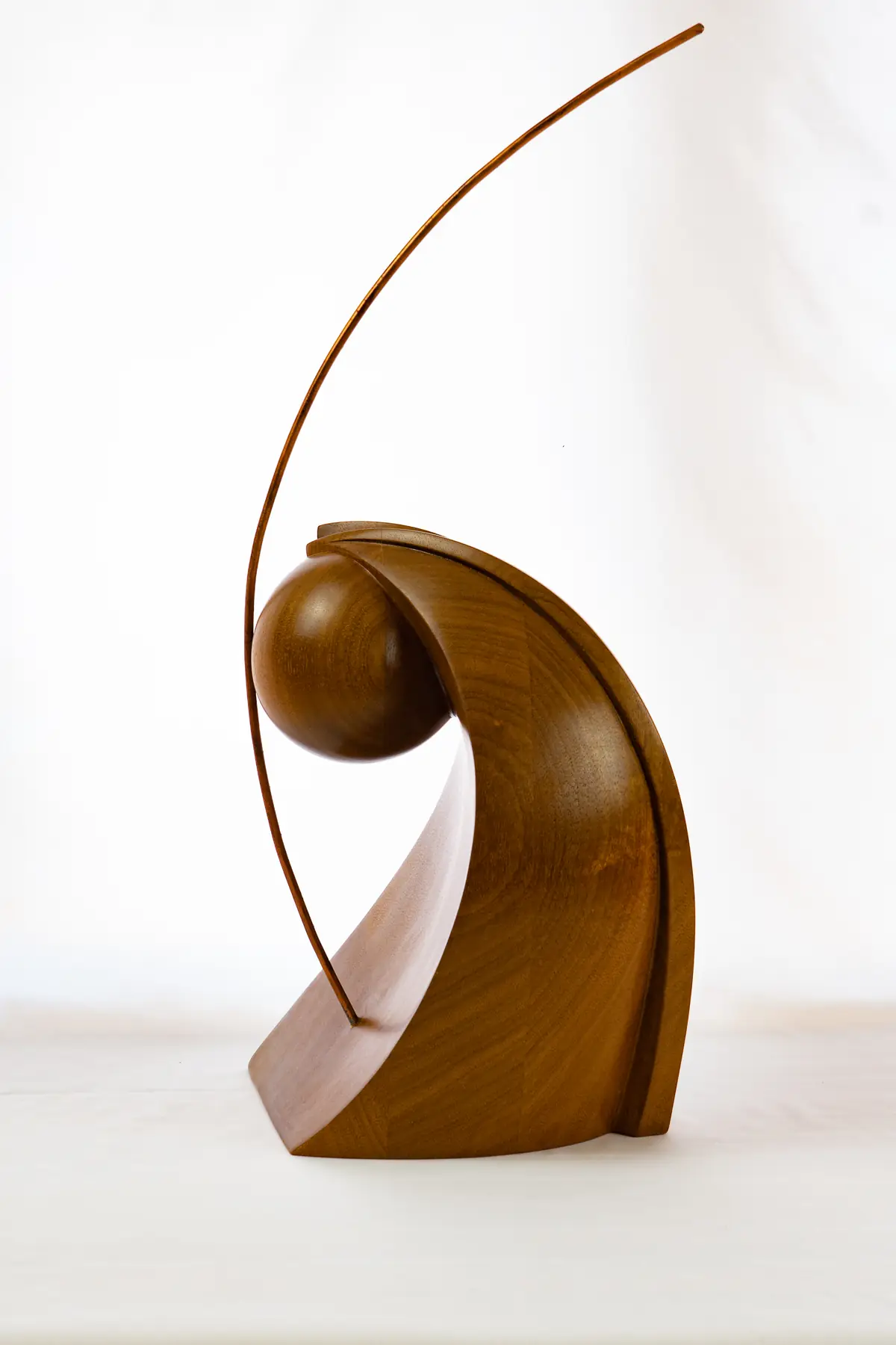 Escultura de madera de sipo con una forma envolvente y una esfera, atravesada por un arco fino de acero