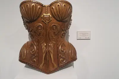Corsé tallado en madera sobre una peana blanca en la sala de exposición, con el relieve de los pliegues y el cierre marcados a gubia