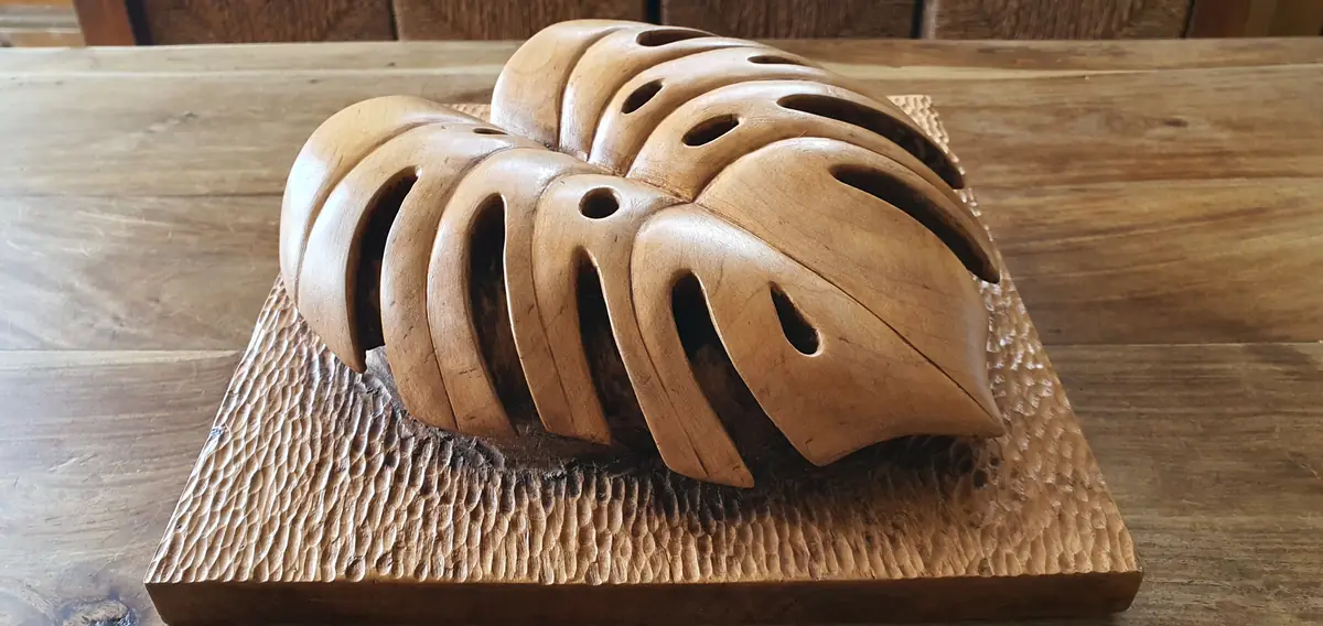 Relieve de una hoja de palma tallado en madera, con nervaduras y aberturas sobre una base rectangular