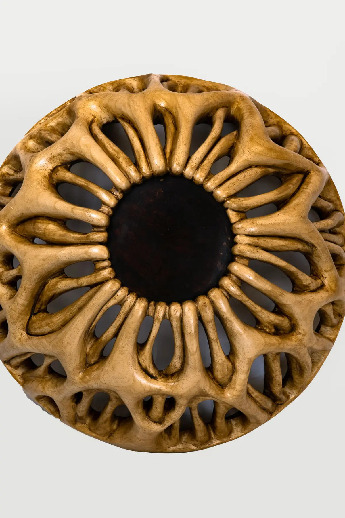 Escultura semiesférica de madera de ayous vista desde arriba, con formas orgánicas radiales alrededor de un centro oscuro